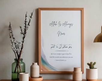 Puede incluir: Un marco de madera rectangular que contiene una impresión blanca con el texto Allah Is Always Near, caligrafía árabe y la traducción al inglés And He is with you wherever you are, Surah Al-Hadid 57:4, con un acento de acuarela colorido.