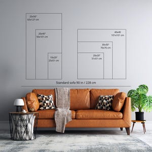 a living room with a brown leather sofa, a coffee table, and a potted plant. The sofa is positioned in front of a wall with two framed size charts providing dimensions for different sofa sizes.