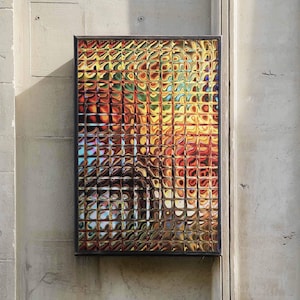 May include: A rectangular wall-mounted sign featuring a grid of square glass panels that create a distorted, prismatic effect. The surface displays a vibrant blend of warm orange, yellow, and red hues, interspersed with cool blue and white light reflections.