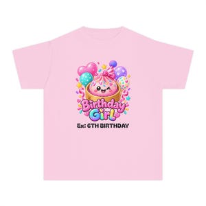 Puede incluir: Una camiseta rosa claro con un gráfico central de una bola de masa sonriente y guiñando un ojo en una vaporera de bambú, usando un sombrero de fiesta. El diseño incluye globos coloridos, confeti y el texto "Birthday Girl" y "Ex: 6TH BIRTHDAY" en negro.