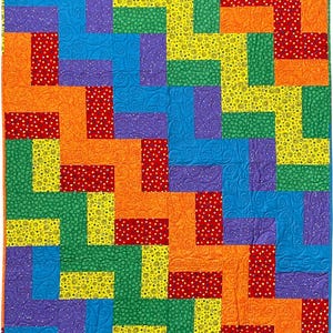 Könnte beinhalten: Ein rechteckiger Quilt mit einem lebendigen geometrischen Muster aus ineinandergreifenden Rechtecken in den Farben Rot, Orange, Gelb, Grün, Blau und Violett. Die Stoffstücke weisen verschiedene Texturen auf, darunter Wirbelmuster und weiße Punkte.