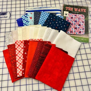 May include: A collection of fabric squares in various colors and patterns, including red, white, and blue, arranged on a grid. A booklet titled "The Wave" is visible, along with a variety of other fabrics, perfect for quilting projects.