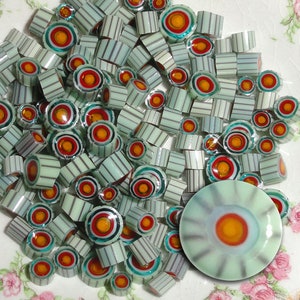 May include: A collection of small, round, glass beads with a striped pattern and a colorful, concentric circle design. The beads are in shades of green, white, orange, and blue.