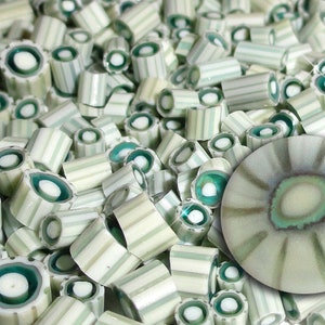 May include: A collection of light green and white striped glass beads and a single, larger, round bead. The beads have a cylindrical shape with a teal-colored center. The larger bead has a similar color scheme with radiating lines.