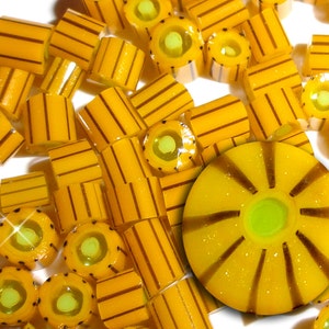May include: A close-up of yellow and brown striped candy with a green center. The candy is arranged in a pile on a white surface.