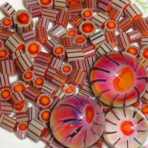 May include: A collection of colorful glass beads with a striped pattern. The beads are arranged in a pile with three larger, round, multi-colored glass marbles with a swirl pattern.