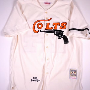 May include: A cream-colored button-down baseball jersey featuring the word COLTS in orange lettering with a black revolver graphic underneath. The shirt includes the text 1964 Jimmy Wynn and a Cooperstown Collection patch on the lower front.