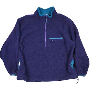 May include: A deep purple fleece pullover with a textured, fuzzy surface. It features a teal stand-up collar, a quarter-length zipper with a purple pull, a small chest pocket with a teal trim, and teal accents at the cuffs and hem with a drawstring.