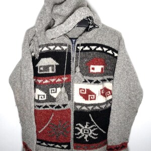 May include: A gray knit zip-up hoodie featuring a multi-colored pattern of houses, geometric shapes, and star-like motifs in black, white, and red. The garment includes long sleeves, a hood with drawstrings, and two front pockets with tassels.