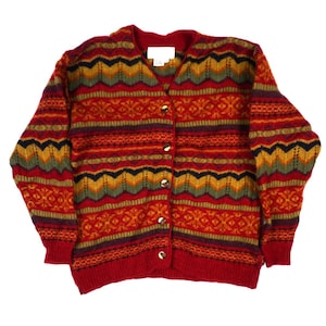 Op de afbeelding: Een vest met lange mouwen en een V-hals, voorzien van een veelkleurig gebreid patroon in de kleuren rood, oranje, geel, groen en donkerblauw. Het kledingstuk heeft een knoopsluiting aan de voorzijde met vijf ronde knopen en geribbelde boorden.