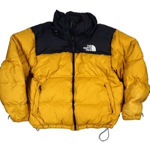 May include: A mustard yellow and black puffer jacket featuring a high collar, a full-length front zipper, and two zippered side pockets. The North Face logo is embroidered in white on the upper left chest, with 700 text on the sleeve.
