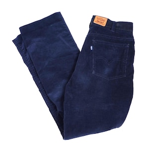 Könnte beinhalten: Dunkelblaue Cordhose mit hoher Taille und einem beigefarbenen Lederaufnäher am hinteren Bund. Die Hose verfügt über eine Gesäßtasche mit einem kleinen weißen Etikett und einem klassischen, bogenförmigen Zierstich auf dem Taschenstoff.
