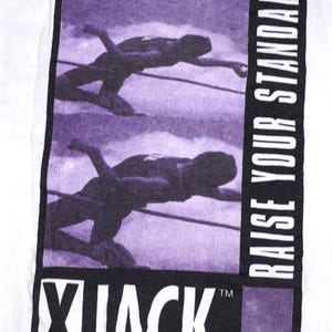 May include: A white t-shirt featuring a rectangular graphic with a purple-toned sequence of a high jumper clearing a bar. The text RAISE YOUR STANDARDS is printed vertically in white on a black border, with the brand name XJACK in bold white letters.