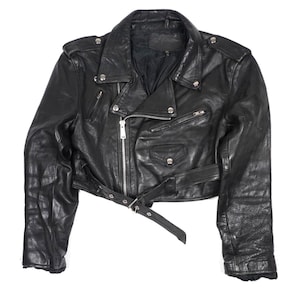May include: A black leather cropped motorcycle jacket featuring a wide notched collar, silver-tone metal zippers, multiple zippered pockets, shoulder epaulets with snap buttons, and an adjustable waist belt with a metal buckle closure.