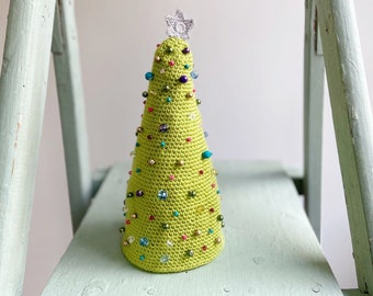 Op de afbeelding: Een limoengroen gehaakte kerstboomversiering versierd met kleurrijke kralen en een zilveren ster bovenop.