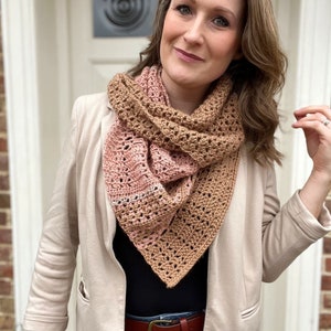 May include: A woman wearing a beige blazer with a crocheted shawl in shades of brown and pink. The shawl is draped around her neck and shoulders, and the ends are tied in a knot at the front.
