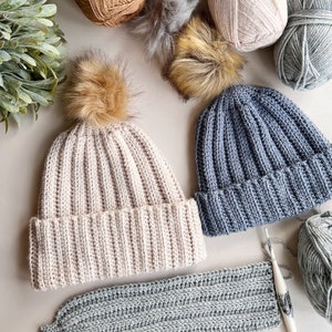 May include: Two crocheted hats, one beige and one blue, with faux fur pom poms.  There are several balls of yarn in various colors, including beige, brown, blue, and green.