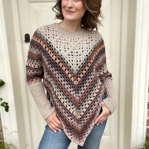 Puede incluir: Un poncho de ganchillo con un patr&oacute;n geom&eacute;trico en tonos marrones, rosas y grises. El poncho tiene mangas largas y un corte holgado.