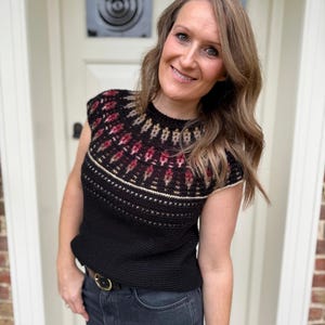 Pu&ograve; includere: Top all'uncinetto nero con carr&egrave; fantasia con disegni geometrici rossi, beige e oro. Il top ha girocollo e maniche corte. La modella indossa jeans scuri e una cintura nera con fibbia dorata.