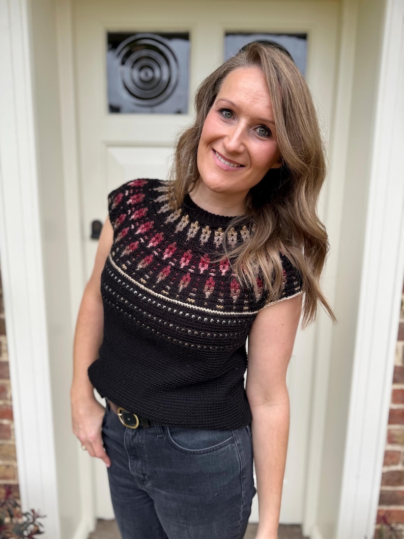 Pu&ograve; includere: Top all'uncinetto nero con carr&egrave; fantasia con disegni geometrici rossi, beige e oro. Il top ha girocollo e maniche corte. La modella indossa jeans scuri e una cintura nera con fibbia dorata.