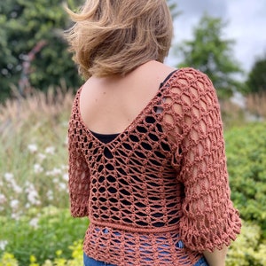 Puede incluir: Un top de crochet con un dise&ntilde;o de tejido abierto y suelto en color terracota. El top tiene cuello en V y mangas 3/4.