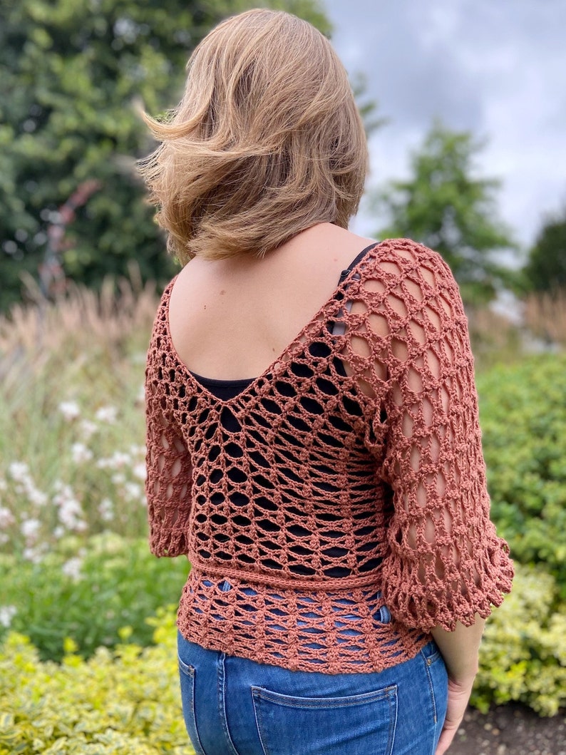 Puede incluir: Un top de crochet con un dise&ntilde;o de tejido abierto y suelto en color terracota. El top tiene cuello en V y mangas 3/4.
