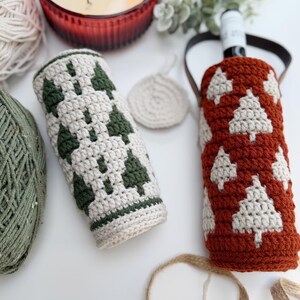 May include: Two crocheted wine bottle covers, one in cream with green tree designs, the other in rust with cream tree designs. A small cream coaster and a candle in a red glass are also visible.