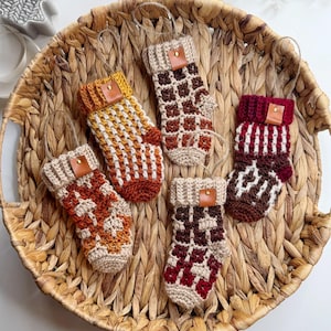 May include: Five crocheted Christmas stockings in a variety of colours, including red, brown, and orange, with a brown leather tag on each stocking.