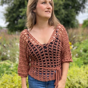Puede incluir: Un top de crochet de color terracota con cuello en V y un lazo en la cintura. El top tiene un patr&oacute;n de encaje y se lleva con jeans azules.