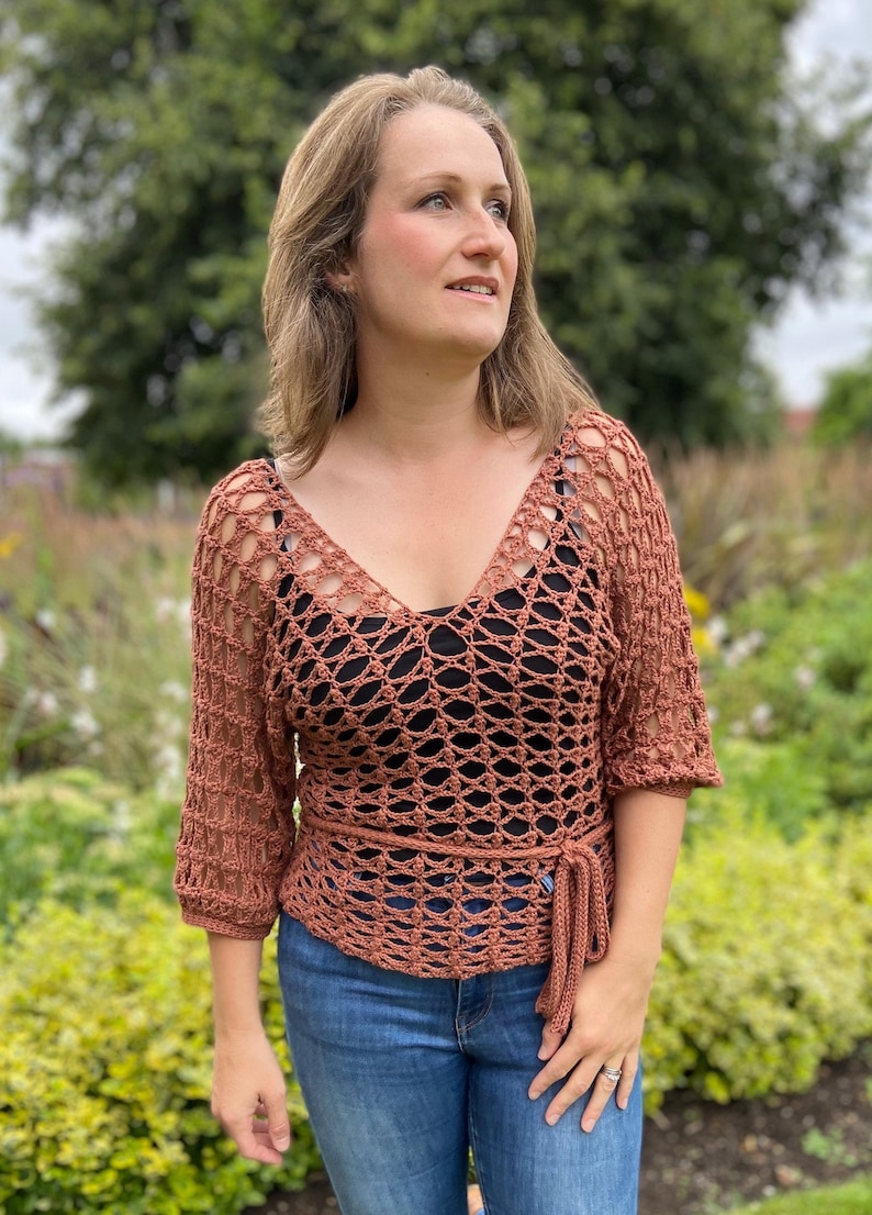 Puede incluir: Un top de crochet de color terracota con cuello en V y un lazo en la cintura. El top tiene un patr&oacute;n de encaje y se lleva con jeans azules.