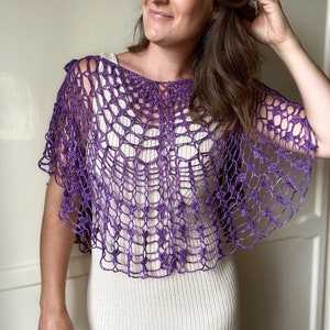 Peut inclure: Un châle en crochet violet avec un motif ajouré délicat. Le châle est porté sur une robe blanche.