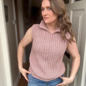 May include: A sleeveless, dusky pink knitted top with a collared neckline. The top has a ribbed texture and is worn with blue jeans. The outfit is casual and suitable for everyday wear.