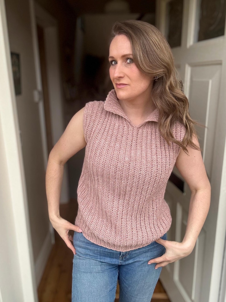 May include: A sleeveless, dusky pink knitted top with a collared neckline. The top has a ribbed texture and is worn with blue jeans. The outfit is casual and suitable for everyday wear.