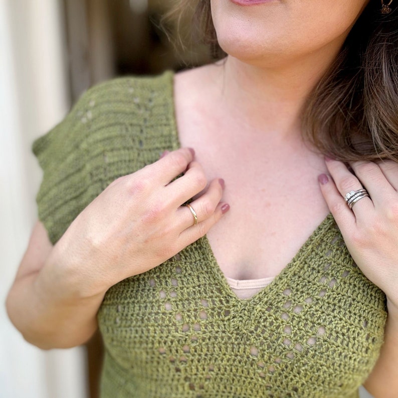 Puede incluir: Primer plano de una mujer con un top de crochet verde con escote en V. Lleva un anillo de oro en el dedo anular izquierdo y un anillo de plata en el dedo anular derecho.