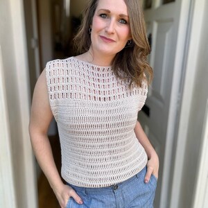 May include: A crocheted sleeveless top with a delicate openwork pattern in a light beige color. The top has a round neckline and a relaxed fit.