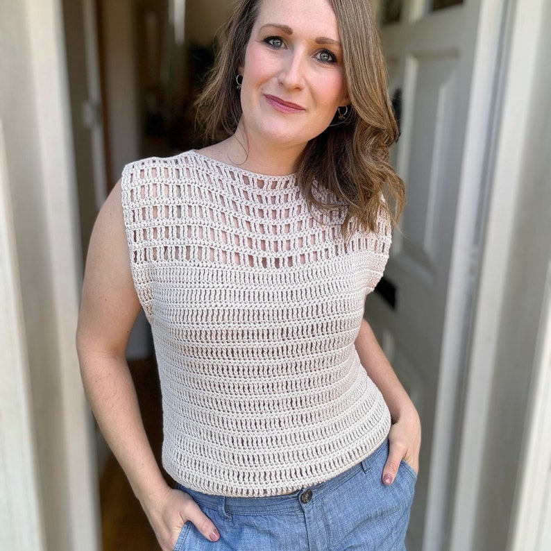 May include: A crocheted sleeveless top with a delicate openwork pattern in a light beige color. The top has a round neckline and a relaxed fit.