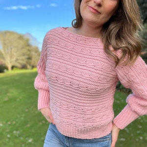 Woman in cable crochet sweater pattern with deep arm cuffs in pink yarn.