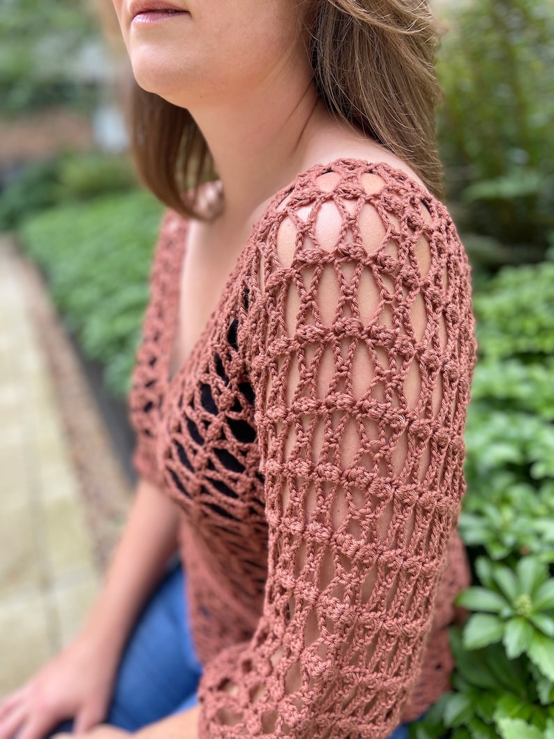 Puede incluir: Un top de crochet de color terracota con un dise&ntilde;o suelto y tejido abierto. El top tiene un cuello en V y mangas tres cuartos.
