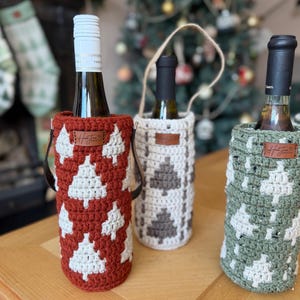 May include: Three wine bottles in decorative crochet bottle holders. The holders are in red, white, and green, with a Christmas tree pattern. Each holder has a leather tag with the brand name.