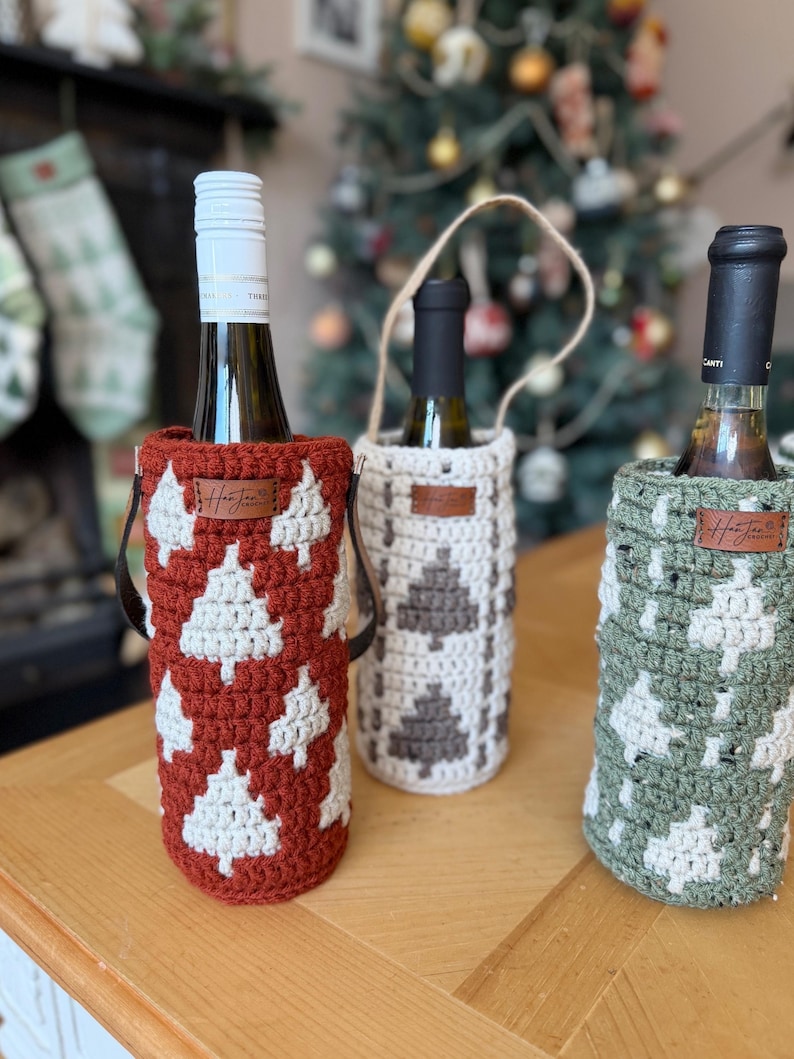 May include: Three wine bottles in decorative crochet bottle holders. The holders are in red, white, and green, with a Christmas tree pattern. Each holder has a leather tag with the brand name.