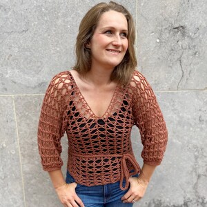 Puede incluir: Un top de crochet de color &oacute;xido con cuello en V y un lazo en la cintura. El top tiene un corte holgado y un delicado patr&oacute;n de calado.