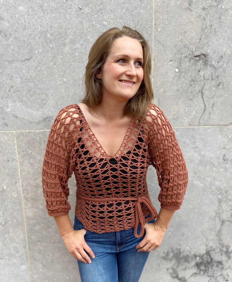 Puede incluir: Un top de crochet de color &oacute;xido con cuello en V y un lazo en la cintura. El top tiene un corte holgado y un delicado patr&oacute;n de calado.