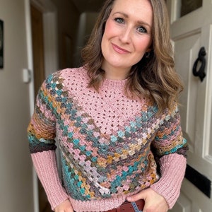 Op de afbeelding: Een roze gehaakte trui met een kleurrijk geometrisch patroon. De trui heeft lange mouwen en een ronde hals.