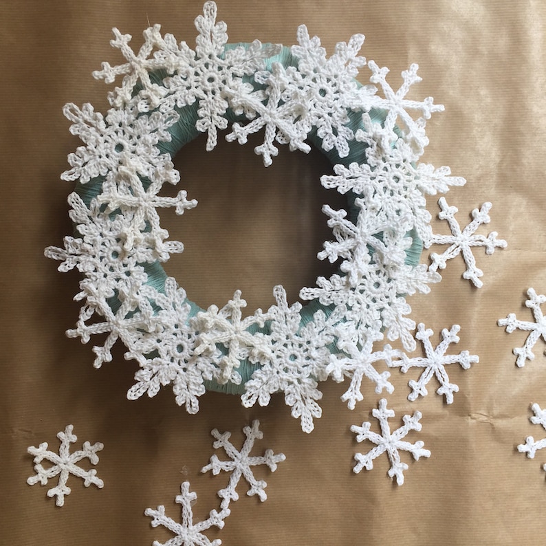 A christmas wreath made out of overlayed crocheted snowflakes. This is being assembled. Wreath is on a wooden background.