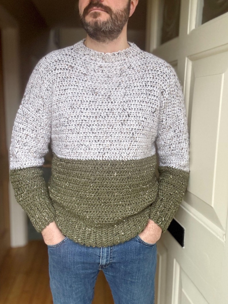 Puede incluir: Un su&eacute;ter tejido a crochet con un esquema de dos colores. La mitad superior del su&eacute;ter es de color gris claro con motas negras, y la mitad inferior es de color verde oscuro con motas doradas.