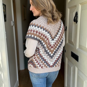 May include: A crocheted vest with a geometric pattern in shades of brown, beige, and gray. The vest has a V-neck and sleeveless design.