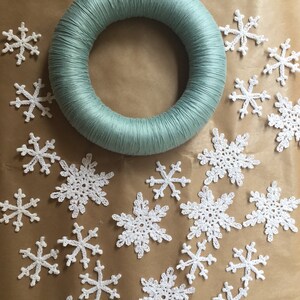 A collection of crocheted snowflakes ready to be assembled on a green christmas wreath.