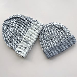 May include: Two crocheted hats in a gray and white color scheme. One hat is folded down and the other is laying flat.