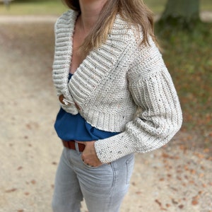 Pu&ograve; includere: Un cardigan in crochet color crema con scollo a V e maniche lunghe. Il cardigan &egrave; corto e ha una texture macchiettata.