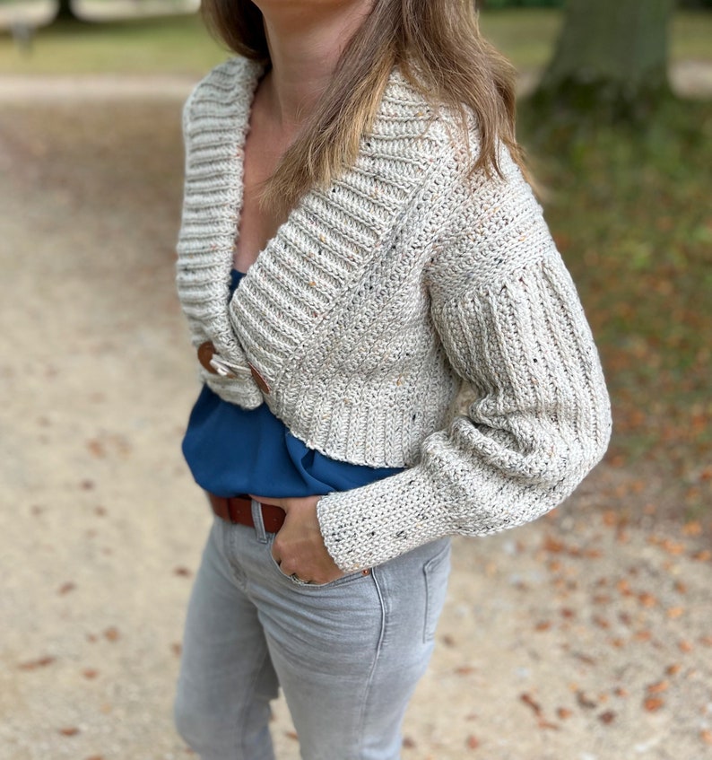 Pu&ograve; includere: Un cardigan in crochet color crema con scollo a V e maniche lunghe. Il cardigan &egrave; corto e ha una texture macchiettata.